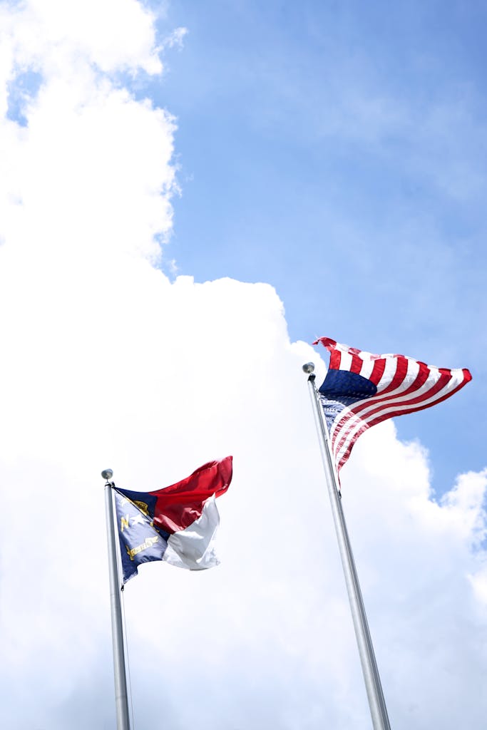Low angle view of American and North Carolina flags waving against a bright blue sky.