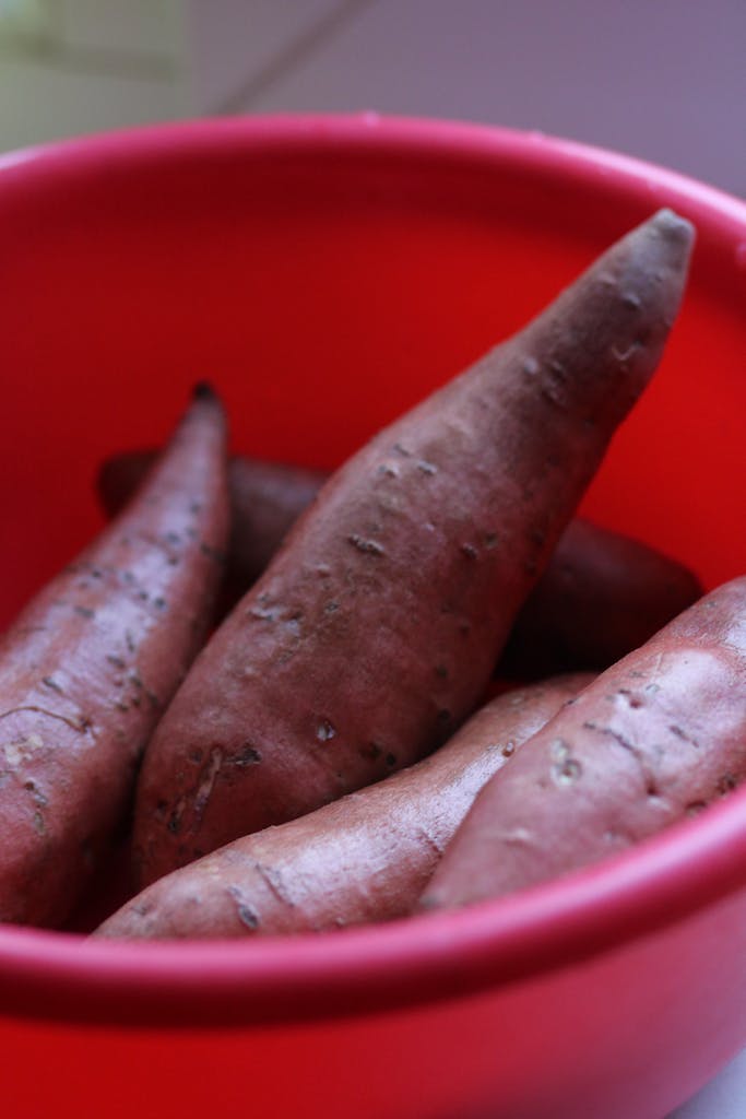 Close-up of fresh sweet potatoes in a red bowl, highlighting rustic charm.